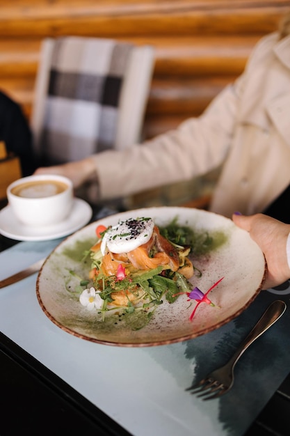 El camarero trae el desayuno para el cliente en la terraza sándwich fresco con salmón y huevo asado en la parte superior