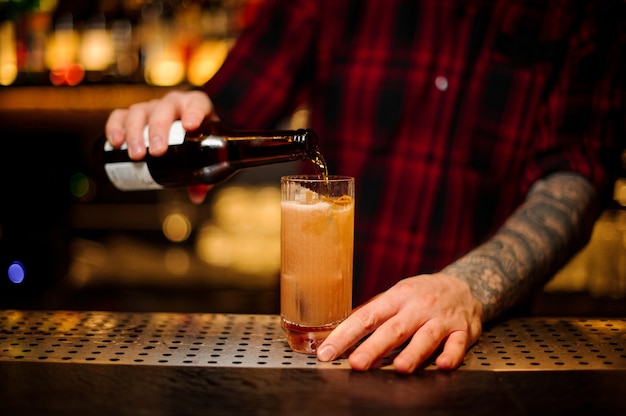 Camarero vertiendo un alcohol en un cóctel Singapore Sling de la botella en la barra del bar