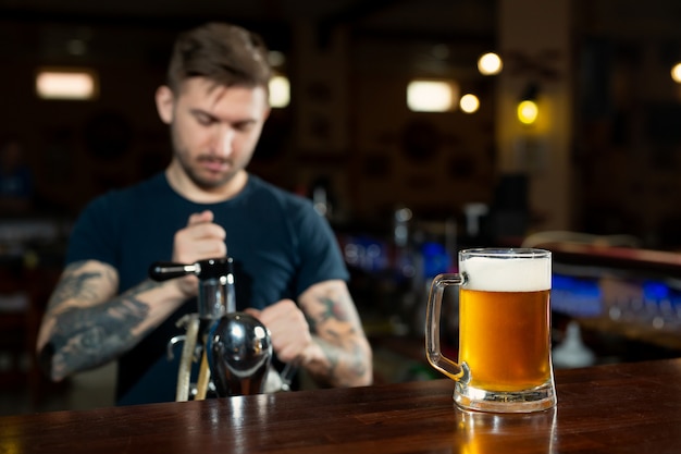 Camarero vertiendo cerveza de barril fresca en el vaso en pub