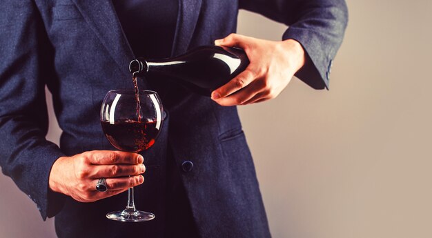 Camarero vertiendo vino tinto en un vaso. Sommelier, degustación, bodega, enólogo masculino. El vino tinto se vierte de botella en copa.