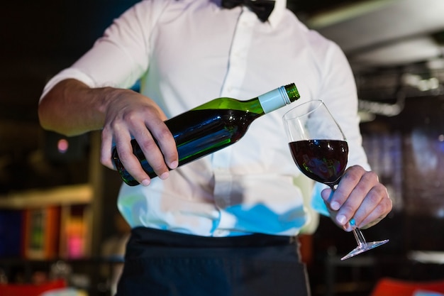 Camarero vertiendo vino en un vaso en el bar