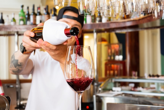 Camarero vierte una copa de vino tinto en el bar