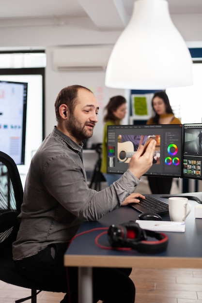 Foto camarógrafo discutiendo en línea con el cliente que tiene un teléfono inteligente para editar imágenes de películas sentado en una agencia creativa