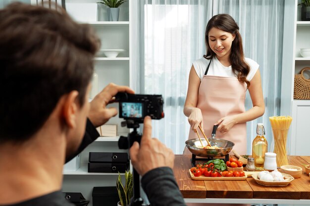 El camarógrafo grabando a la mujer en el chef influyente cocinando espagueti Postulado