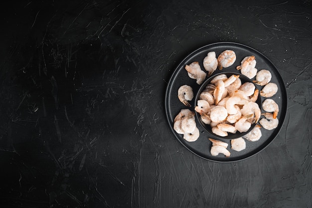 Camarones congelados rosados con hielo. Mariscos pelados crudos, en un tazón, sobre una mesa de piedra negra, vista superior plana