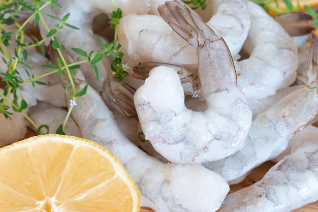 Camarones crudos congelados pelados en una tabla de cortar de madera con hierbas y limón