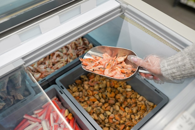 Camarones crudos rosados congelados en caja. Mano de mujer sostiene camarones frescos. Mariscos crudos sin pelar