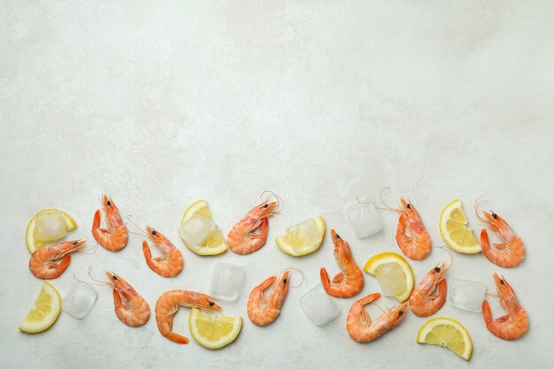 Camarones, cubitos de hielo y rodajas de limón sobre textura blanca