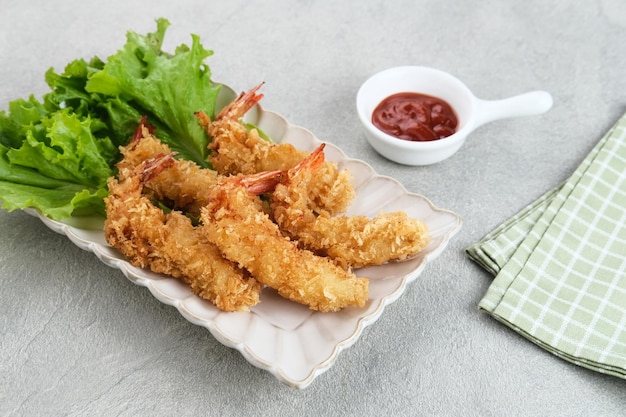 Camarones empanizados fritos con vegetales en un plato servido con salsa picante