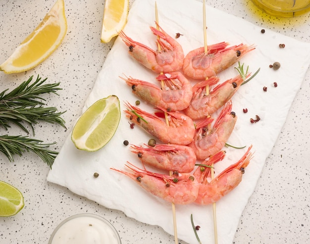 Camarones ensartados en palos de madera, salsa de soja y especias en una vista superior de la mesa blanca