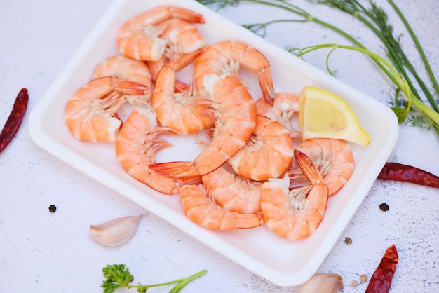 Foto camarones frescos en una bandeja de plástico con hierbas y especias, chile limón sobre fondo blanco, gambas hervidas, comida cocinada en el restaurante de mariscos