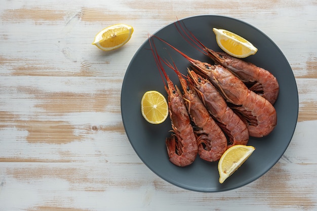 Camarones frescos en placa de madera con rodaja de limón.