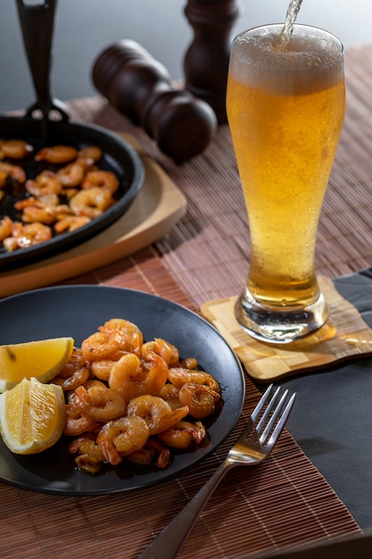 Camarones fritos y limón en un plato negro con vaso de cerveza