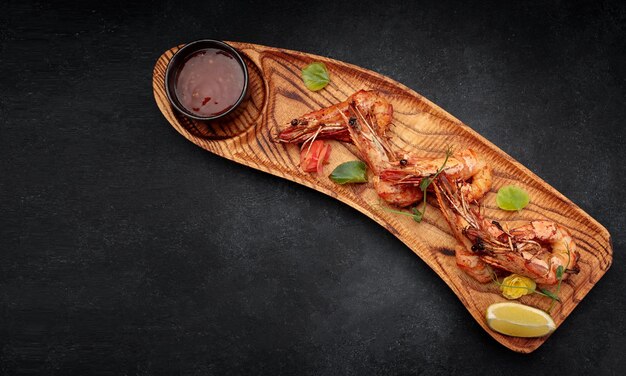 Camarones fritos a la parrilla con salsa de ajo sobre una tabla de madera sobre un fondo oscuro