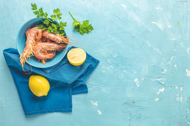 Camarones, gambas con perejil en placa de cerámica azul rodeada de servilleta y limón sobre una superficie de mesa de hormigón azul claro clásico