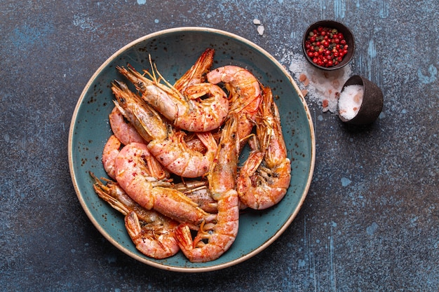 Camarones grandes fritos enteros en un tazón azul con sal y pimienta sobre fondo rústico de piedra desde arriba. Camarones a la parrilla deliciosos cocidos frescos servidos en la vista superior de la placa, comida saludable de mariscos