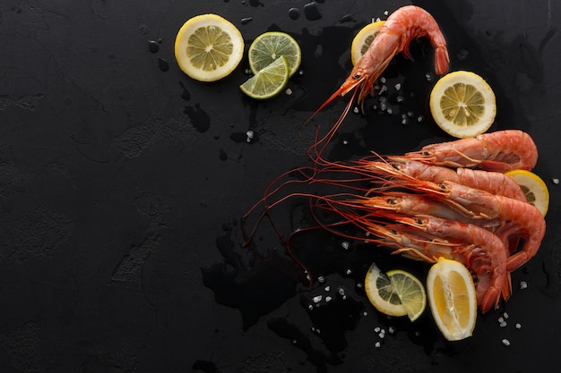 Camarones hervidos con limón sobre fondo negro, copie el espacio. Vista superior de apetitosos bocadillos de mariscos, servicio de restaurante.