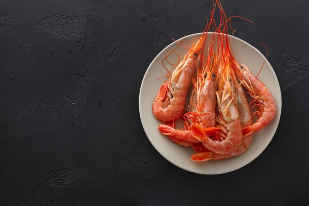 Camarones hervidos en un plato blanco sobre fondo negro, copie el espacio. Vista superior de apetitosos bocadillos de mariscos, servicio de restaurante.