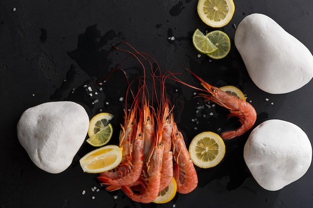 Camarones con limón y piedras blancas sobre fondo negro, copie el espacio. Vista superior de apetitosos bocadillos de mariscos, servicio de restaurante.