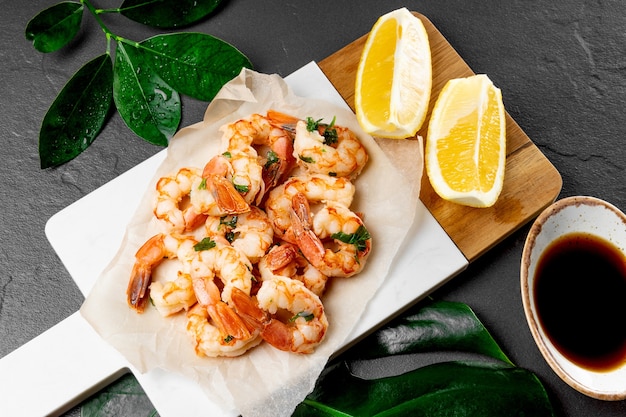 Camarones con limón y salsa de soja sobre una tabla de cortar blanca y verde monstera dejar, cerrar