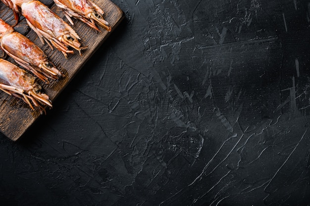 Camarones de mariscos en tabla de cortar de madera sobre superficie de hormigón negro
