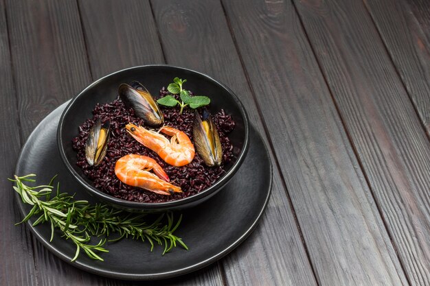 Camarones y mejillones con arroz negro en bol. Vista superior. Mesa de madera oscura.