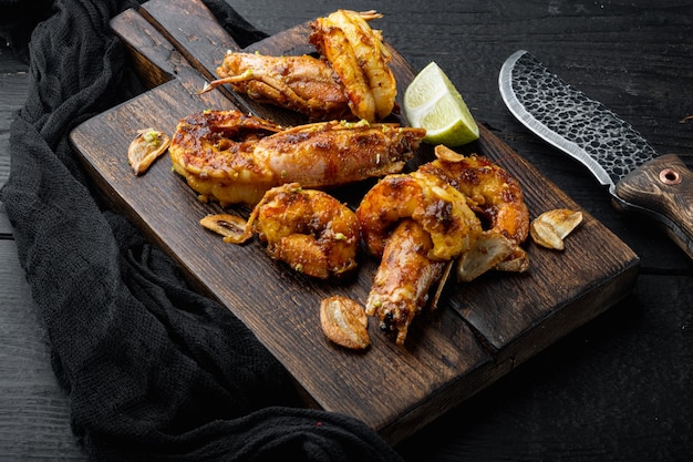 Camarones a la parrilla o langostinos servidos con chutney de mango crujiente de ajo, sobre tabla de madera, sobre mesa de madera negra