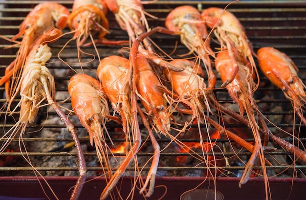 Camarones a la parrilla, pescados y mariscos a la parrilla en la estufa de carbón para la venta en el mercado tailandés de comida callejera