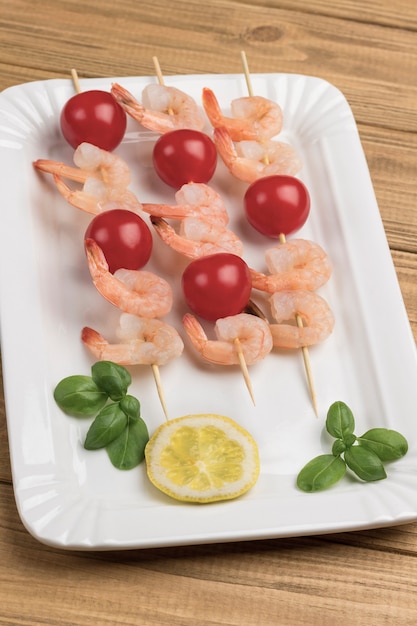 Camarones con pepino y tomates en brocheta en plato blanco.