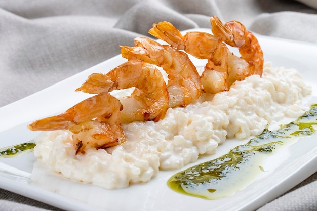 Camarones con risotto y pesto en un plato blanco sobre un fondo textil