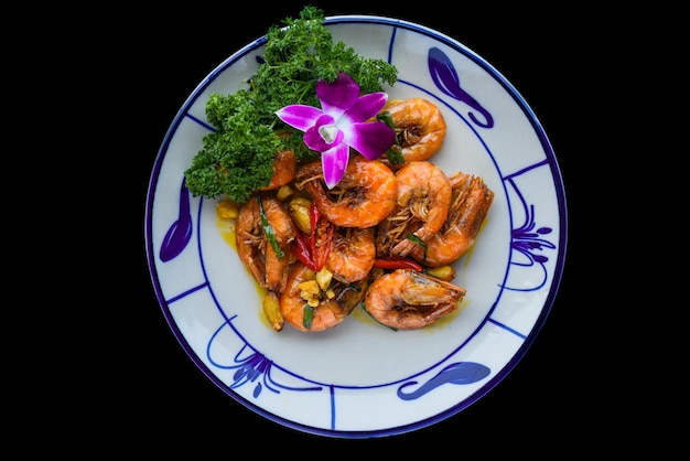 Camarones salteados con salsa y verduras aisladas en el fondo negro