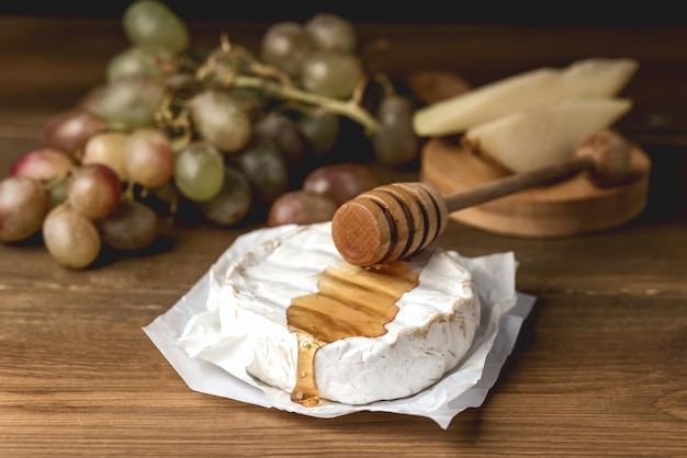 Camembert Brie com mel e uva em fundo de madeira queijo macio e frutas na placa de madeira