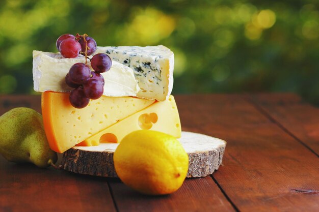 Camembert brie queso duro y uvas en soporte de madera Piezas de queso pera y limón