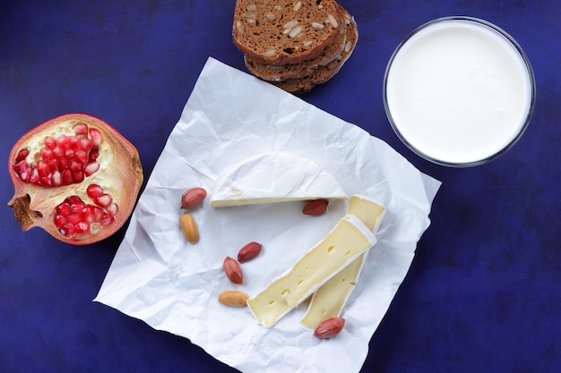 Camembert com pão escuro de nozes e um copo de leite em um fundo azul Um ótimo produto para um café da manhã Delicioso queijo em papel pergaminho closeup