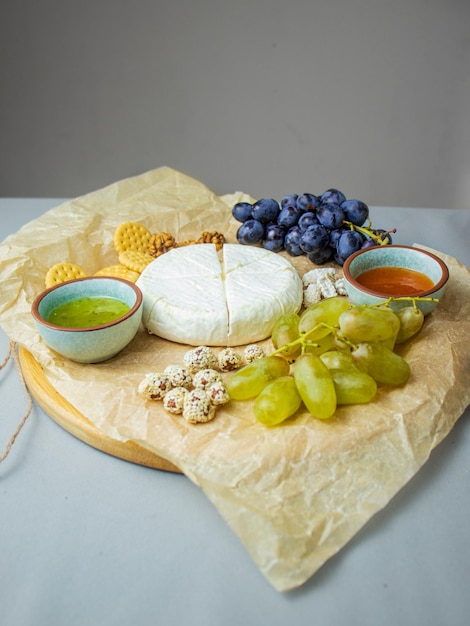 Foto camembert e queijo brie em um fundo rústico com uvas, nozes, geleia e biscoitos, comida italiana