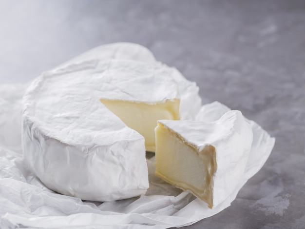 Camembert em um fundo de cimento cinza. Queijo de pasta mole com mofo branco sobre papel manteiga. Copie o espaço. Vista do topo