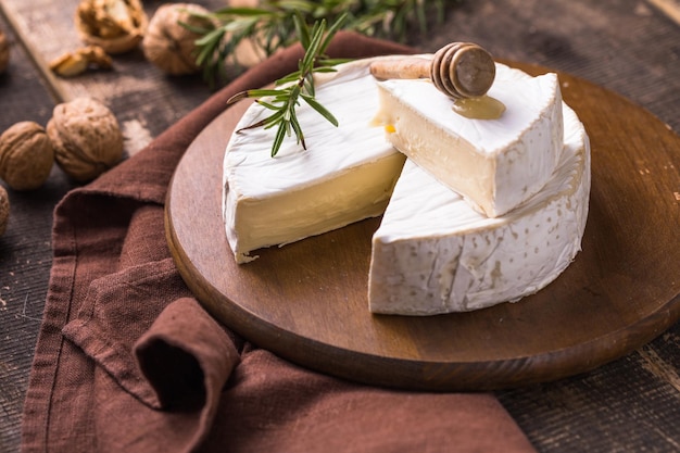 Camembert de granja orgánica o queso brie sobre una tabla de madera con romero y nueces, miel.