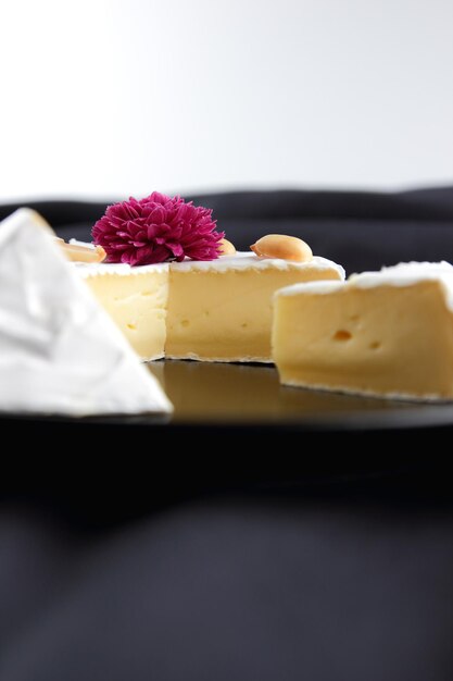 Camembert mit Nüssen auf einem schwarzen Teller Nahaufnahme von Käse mit Rosenblüten und Honig auf schwarzem Hintergrund