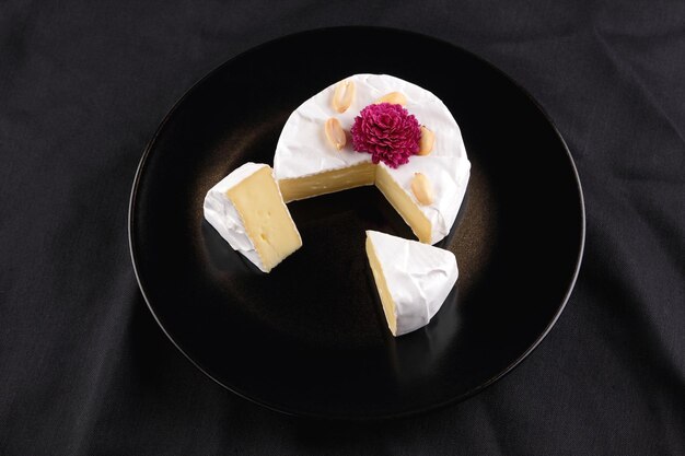 Camembert mit Nüssen und einer Rose Blume auf einem schwarzen Teller Nahaufnahme von Käse auf schwarzem Hintergrund