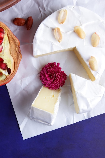 Camembert con nueces y bayas sobre papel pergamino blanco Primer plano de queso con una flor rosa sobre un fondo azul