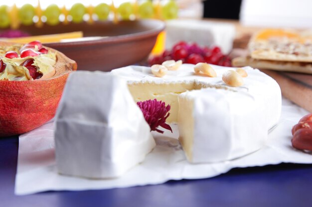 Camembert con nueces y bayas sobre papel pergamino blanco Primer plano de queso con una flor rosa sobre un fondo azul