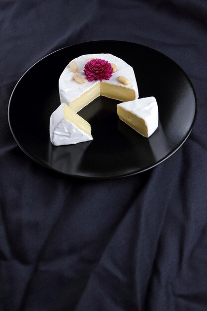 Camembert con nueces y una flor de rosa en un plato negro Primer plano de queso sobre un fondo negro