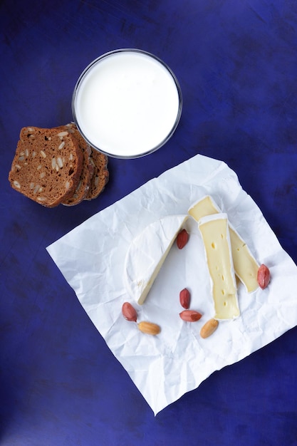 Camembert con nueces, pan oscuro y un vaso de leche sobre un fondo azul. Un gran producto para el desayuno. Delicioso queso en papel pergamino.