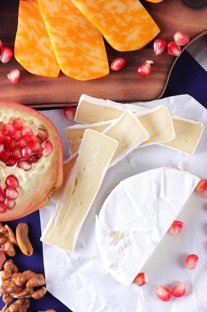 Camembert y queso amarillo duro con granada y nueces sobre un fondo azul Queso sobre tablas de madera