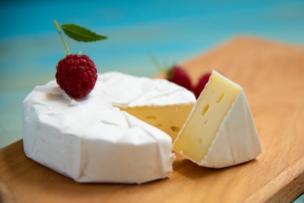 Camembert de queso con frambuesas y uvas sobre un fondo azul.