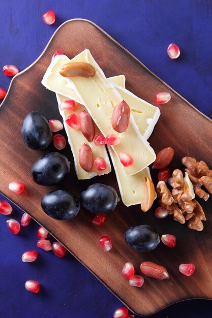 Camembert-Scheiben mit Granatapfelkernen dunklen Trauben und Nüssen auf blauem Hintergrund Köstlicher Käse auf einem Holzbrett Nahaufnahme