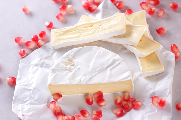 Camembert y semillas de granada sobre papel pergamino sobre un fondo claro Delicioso queso en el primer plano de la mesa Un gran producto para el desayuno