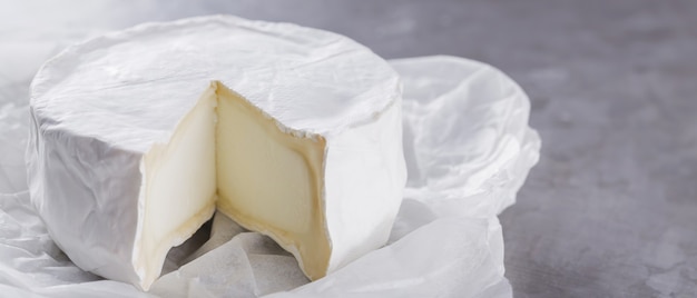 Camembert sobre un fondo de cemento gris. Queso de pasta blanda con moho blanco sobre papel pergamino. Copie el espacio. Vista superior