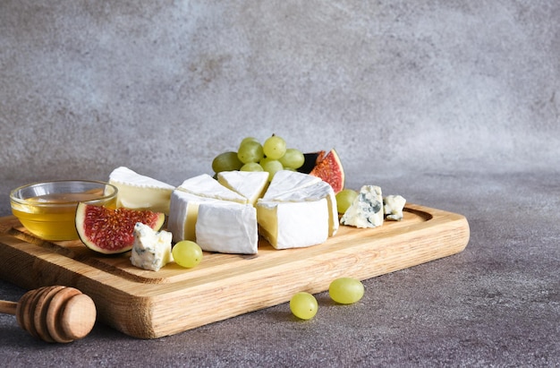 Foto camembertkäse und blauschimmelkäseplatte mit trauben, feigen, honig auf einem holzbrett. käseplatte