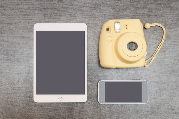 Câmera amarela, um tablet e smartphone em uma mesa preta. Vista do topo